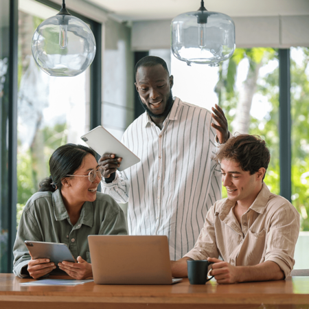 Three people with tablets, laptop and coffee smiling